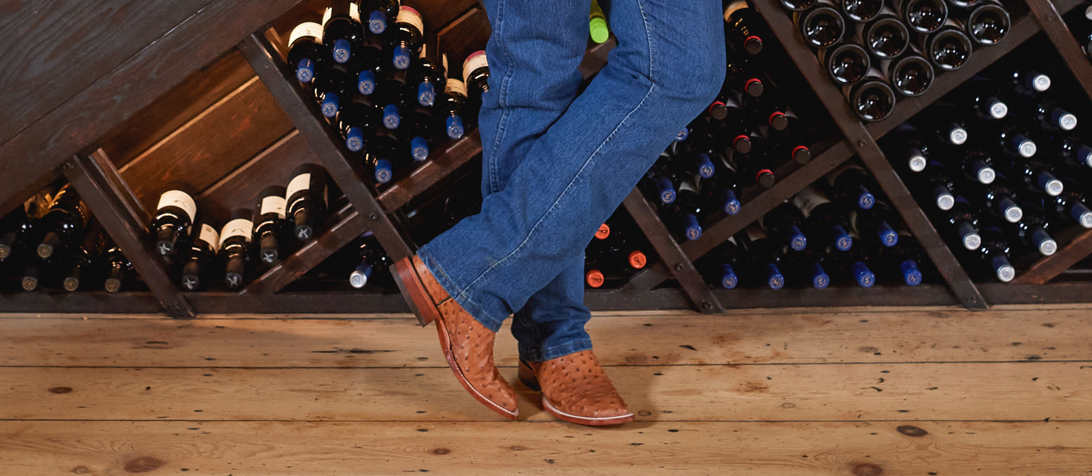 A man wearing Justin Western Boots while standing in front of a wine rack.